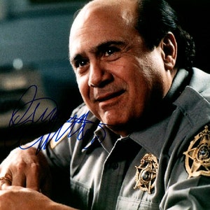 Może przedstawiać: Średnie ujęcie mężczyzny w jasnoszarym mundurze z odznaką i złotym pierścieniem. Mężczyzna uśmiecha się i patrzy w bok. Mundur ma odznakę na ramieniu i odznakę w kształcie gwiazdy na piersi. Obraz jest podpisany niebieskim tuszem.