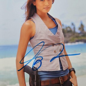May include: A photograph of a person wearing a light gray vest over a blue top, paired with dark jeans and a brown belt. A black holster with a gun is attached to the belt. The background shows a beach and ocean.
