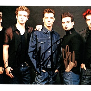 May include: A black and white photo of five men in a band. They are all wearing casual clothing and have their arms around each other. The men are smiling and looking at the camera. The photo is signed by all five members of the band.