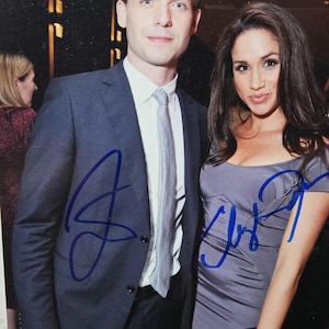 Può includere: Una foto a colori di due persone, un uomo e una donna, in piedi uno accanto all'altra. L'uomo indossa un abito blu scuro con una cravatta grigio chiaro. La donna indossa un vestito grigio. Entrambi hanno firmato i loro nomi con inchiostro blu.