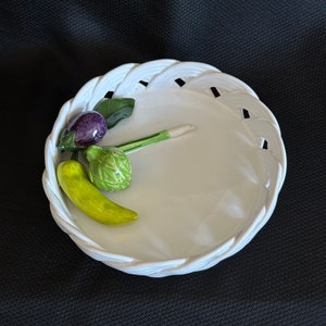 May include: White ceramic bowl with a woven design, featuring three small ceramic vegetables: a green pepper, an artichoke, and an aubergine.