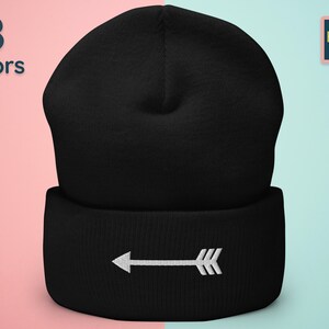 Puede incluir: Gorro negro con una flecha blanca que apunta hacia la izquierda bordada en el puño.