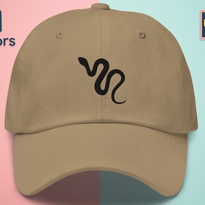 Op de afbeelding: Een beige baseballpet met een zwart geborduurd slangontwerp. De pet heeft een gebogen klep en een verstelbare band.