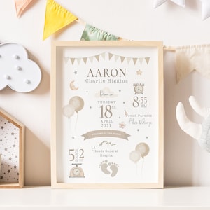 May include: A framed print with a beige background and a cute illustration of a baby's birth announcement. The print includes the baby's name, Aaron Charlie Higgins, birth date, time, weight, and hospital. The print is surrounded by a wooden frame and is displayed on a shelf with other baby decor.