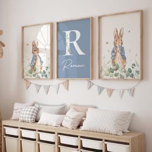 May include: Three framed prints with a blue background and a white letter R, the name Roman, and a watercolor illustration of Peter Rabbit in a blue jacket standing in a field of green leaves.