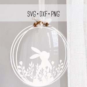 May include: White silhouette of a rabbit in a circle with white floral designs. The circle is hanging from a white string.