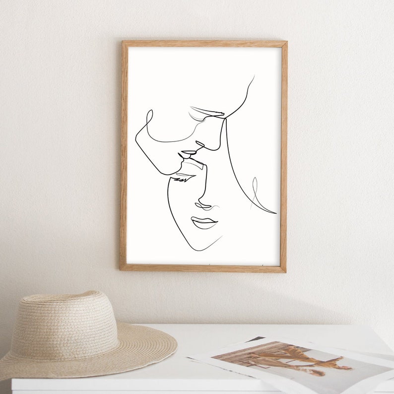May include: A black and white line drawing of two faces, one above the other, with their foreheads touching. The drawing is framed in a light wood frame.