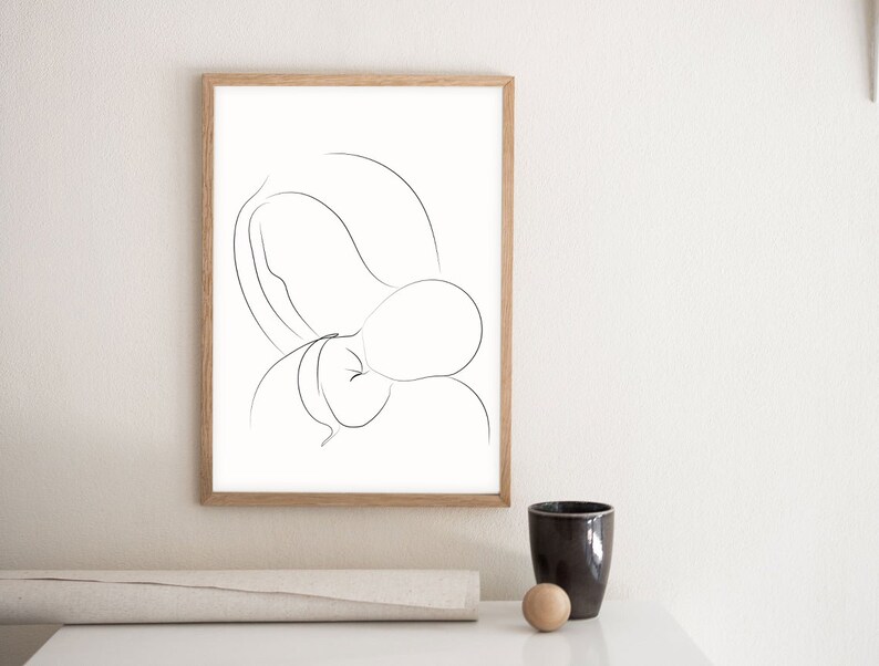 May include: A black and white line drawing of a mother and child in a minimalist style. The drawing is framed in a light wood frame and is hanging on a white wall.