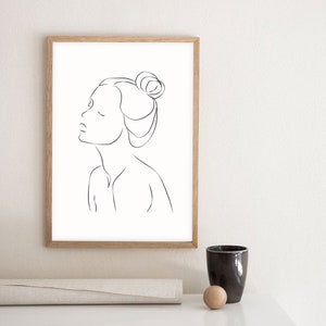May include: A black and white line drawing of a woman's face with her hair pulled back in a bun. The drawing is in a simple, minimalist style.