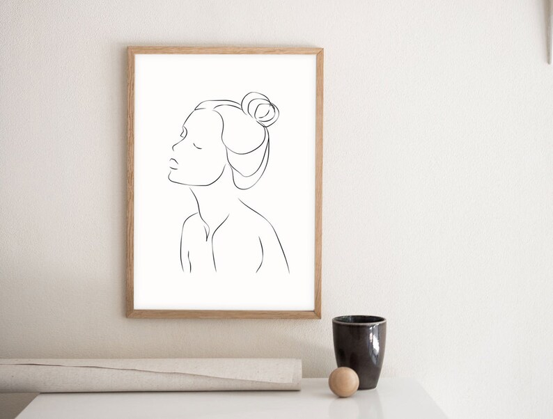May include: A black and white line drawing of a woman's face with her hair pulled back in a bun. The drawing is in a simple, minimalist style.