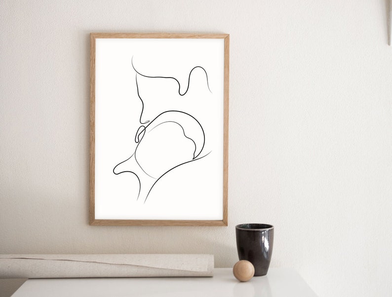 May include: A black and white line drawing of two figures embracing, printed on white paper and framed in a light wood frame.