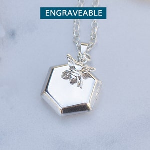 Może przedstawiać: Srebrny naszyjnik z sześciokątnym medalionem i zawieszką w kształcie pszczoły. Medalion jest grawerowany.