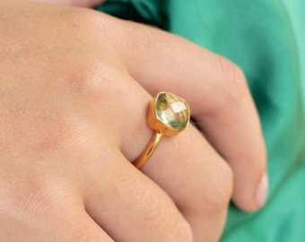May include: A gold ring with a large, light green gemstone. The ring is on a person's finger.