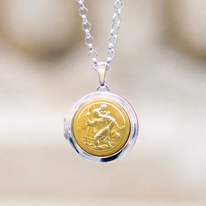 Op de afbeelding: Een zilveren ketting met een ronde hanger. De hanger heeft een goudkleurig medaillon met een gedetailleerd reliëf van een figuur die een andere figuur draagt. De ketting is gemaakt van kleine, verbonden zilveren stukjes.