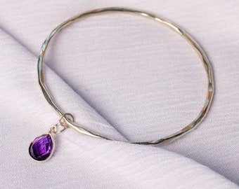 May include: A silver bangle bracelet with a hammered finish and a dangling amethyst gemstone charm.