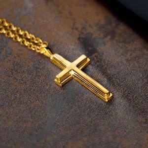 May include: A gold chain necklace with a gold cross pendant. The cross has a simple design with three raised lines.