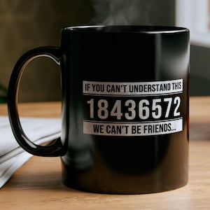 Puede incluir: Taza de cerámica negra con texto blanco que dice "Si no puedes entender esto 18436572 no podemos ser amigos..." La taza está llena de una bebida caliente y sale vapor de la parte superior.