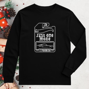 May include: Black long-sleeve shirt with a white graphic that resembles a toy car package. The graphic includes the text "just one more" and "I promise" with a car silhouette. The shirt is a crew neck.
