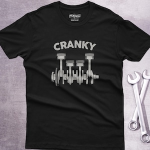 May include: Black t-shirt with the word "CRANKY" above a detailed engine graphic. Two silver wrenches are crossed at the bottom right. The shirt is made of 100% cotton.
