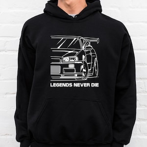 Puede incluir: Sudadera con capucha negra con un gráfico blanco de un coche deportivo y el texto "LEGENDS NEVER DIE". El gráfico del coche es un dibujo lineal detallado de la parte delantera y lateral del vehículo.