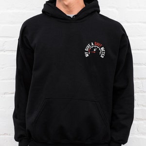Könnte beinhalten: Schwarzer Kapuzenpullover mit einem Grafikdesign auf der linken Brust. Das Design zeigt eine Tankanzeige mit dem Text "MY GIVE A SHIT METER". Der Zeiger der Anzeige zeigt auf leer.