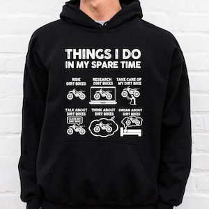 May include: A black hoodie featuring a white graphic that reads "Things I do in my spare time". The graphic depicts a series of illustrations of dirt bikes, including riding, researching, taking care of, talking about, thinking about, and dreaming about dirt bikes.