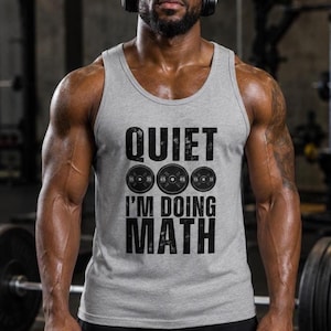 Puede incluir: Una camiseta de tirantes gris claro con el texto en negro QUIET I'M DOING MATH, que incluye tres gráficos circulares de discos de pesas situados entre las palabras, cada uno mostrando valores numéricos de peso en su superficie.