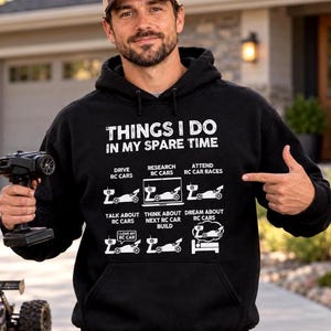 May include: A black hooded sweatshirt featuring white text that reads THINGS I DO IN MY SPARE TIME, followed by six graphic icons depicting activities related to RC cars, including driving, researching, racing, talking, building, and dreaming.