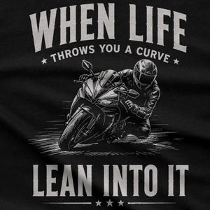 May include: A black t-shirt featuring a white graphic of a motorcyclist leaning into a turn on a sportbike. The text reads "WHEN LIFE THROWS YOU A CURVE" above the motorcycle and "LEAN INTO IT" below, accented with small star icons.