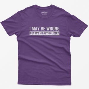 May include: A purple short-sleeved t-shirt featuring the white text "I MAY BE WRONG BUT IT'S HIGHLY UNLIKELY" printed across the chest. The shirt has a crew neckline and a standard fit, with a small interior label visible at the collar area.