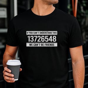 May include: A black short-sleeved t-shirt featuring white text that reads IF YOU CAN'T UNDERSTAND THIS 13726548 WE CAN'T BE FRIENDS. The design is centred on the chest with a rectangular border above and below the numerical sequence.