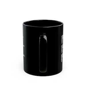 Puede incluir: Una taza de cer&aacute;mica negra s&oacute;lida con un asa vertical y un dise&ntilde;o gr&aacute;fico blanco en el lateral. El dise&ntilde;o incluye una columna de tres iconos de chanclas blancas y texto blanco parcialmente visible impreso en el lado izquierdo de la taza.