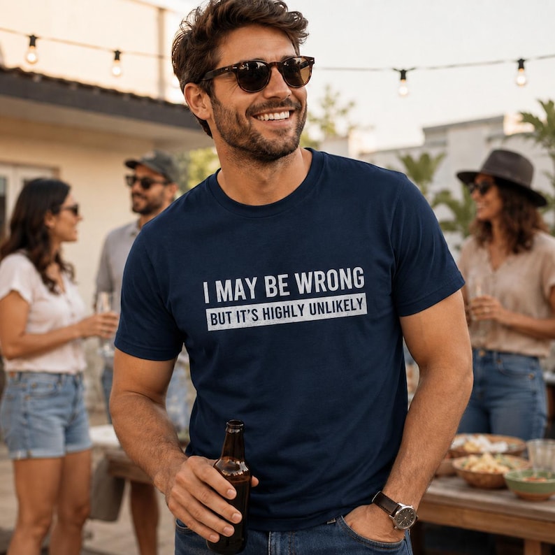 May include: A navy blue short-sleeved t-shirt featuring the white text "I MAY BE WRONG" on the top line and "BUT IT'S HIGHLY UNLIKELY" on the bottom line, with the bottom text enclosed in a white rectangular box.