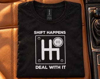 Pode incluir: Uma t-shirt preta com um gráfico branco de um padrão de mudanças manual. O texto SHIFT HAPPENS está impresso acima do gráfico e o texto DEAL WITH IT está impresso abaixo numa fonte branca, em negrito e sem serifas.