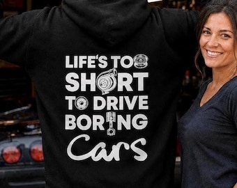May include: A black hooded sweatshirt featuring white text on the back that reads "LIFE'S TOO SHORT TO DRIVE BORING Cars." The design includes white graphic illustrations of a turbocharger, a wheel, and a piston integrated into the lettering.