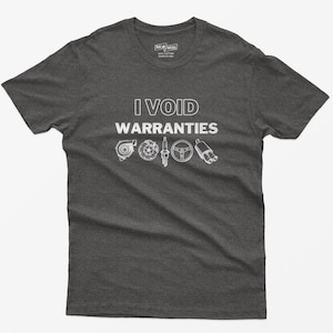 May include: A dark grey t-shirt with the text "I VOID WARRANTIES" in white. The shirt features a graphic of car parts, including a turbocharger, spark plugs, a steering wheel, and an exhaust pipe.