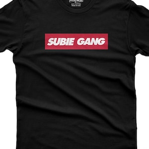 Op de afbeelding: Een zwart t-shirt met korte mouwen en een rechthoekige rode afbeelding op de borst met de witte tekst SUBIE GANG. Het label in de nek bevat de tekst 365CAR MODS, 100% COTTON en MADE IN USA. Het t-shirt is voorzien van een ronde halslijn.