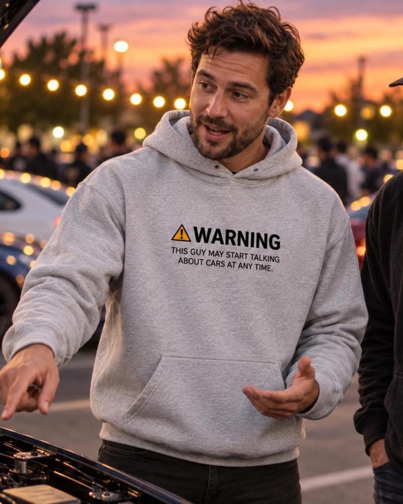 Man in a sports grey car guy warning hoodie talking to friends next to an open engine bay at an evening car meet