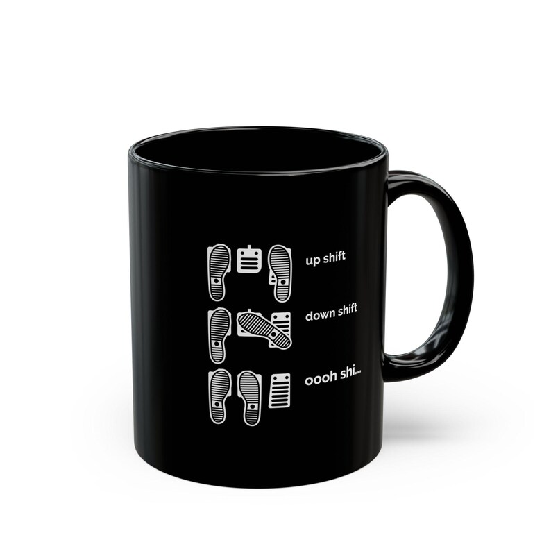 Puede incluir: Una taza de cer&aacute;mica negra con un gr&aacute;fico blanco de tres filas de pedales de coche y posiciones de pies. El texto dice up shift, down shift y oooh shi... junto a las configuraciones de pedales para un veh&iacute;culo de transmisi&oacute;n manual.