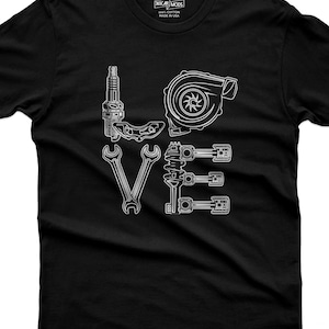 May include: A black short-sleeve t-shirt featuring a white graphic design that spells the word LOVE using automotive parts. The L is a spark plug, the O is a turbocharger, the V is two wrenches, and the E is a strut with three pistons.