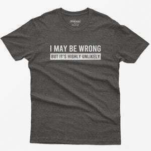 May include: A dark heather gray short-sleeve t-shirt featuring the white text "I MAY BE WRONG BUT IT'S HIGHLY UNLIKELY" printed across the chest. The shirt has a crew neckline and a standard fit, with a small brand label visible at the inner neck.