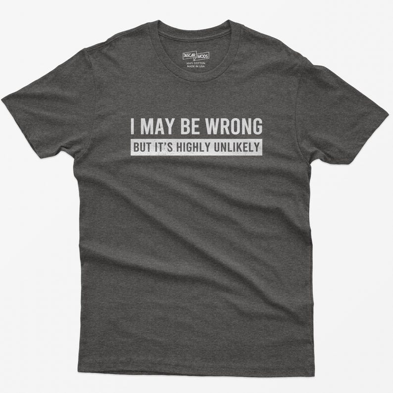 May include: A dark heather gray short-sleeve t-shirt featuring the white text "I MAY BE WRONG BUT IT'S HIGHLY UNLIKELY" printed across the chest. The shirt has a crew neckline and a standard fit, with a small brand label visible at the inner neck.