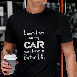 Puede incluir: Una camiseta negra de manga corta con texto en blanco que dice: I work Hard so my CAR can have a Better Life. La palabra CAR está impresa en una fuente más grande, negrita y estilizada, mientras que el resto del texto está en una fuente blanca sencilla.