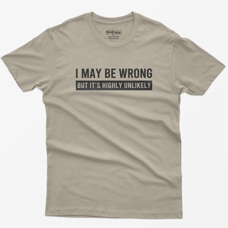May include: A light tan short-sleeved crew neck t-shirt featuring the black text I MAY BE WRONG BUT IT'S HIGHLY UNLIKELY printed across the chest. The interior neck label displays the brand name WSCAR MODS and indicates 100% cotton made in USA.