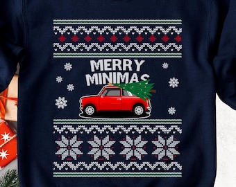 May include: A navy blue long-sleeve sweatshirt featuring a graphic of a red car carrying a green Christmas tree on its roof. The text MERRY MINIMAS is printed above the car, surrounded by white snowflake patterns and red geometric borders.