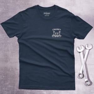 Op de afbeelding: Een marineblauw t-shirt met korte mouwen en een kleine witte afbeelding op de linkerborst. De afbeelding toont een krukas met zuigers en de tekst CRANKY erboven. Het shirt heeft een ronde hals en een label in de kraag met CAR MODS.