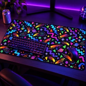 May include: A rectangular desk mat featuring a black background with a vibrant, multi-colored space-themed pattern of planets, stars, comets, and neon geometric shapes, including zig-zags and triangles, with a black mechanical keyboard and mouse.
