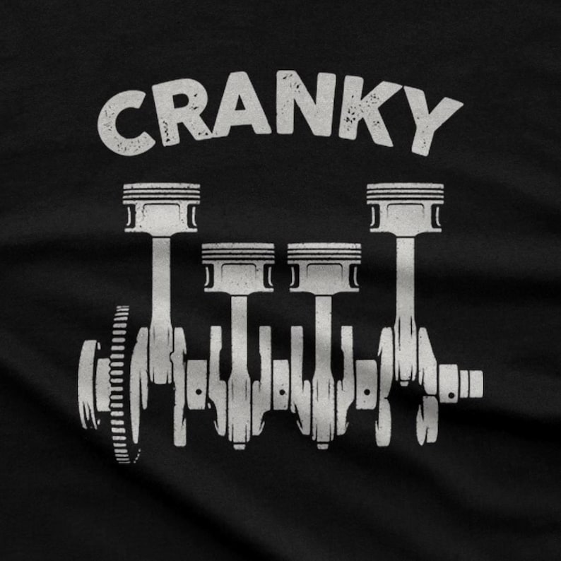 Op de afbeelding: Een zwart t-shirt met een witte grafische print van een viercilinder motor-krukas met zuigers. Het woord CRANKY is in een verweerd wit lettertype boven de mechanische illustratie op de stof gecentreerd afgedrukt.