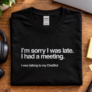 Puede incluir: Una camiseta negra de cuello redondo con texto en blanco que dice: I'm sorry I was late. I had a meeting. I was talking to my ChatBot. La camiseta tiene una etiqueta de la marca Gildan en el cuello interior que indica talla L y 100% algodón.