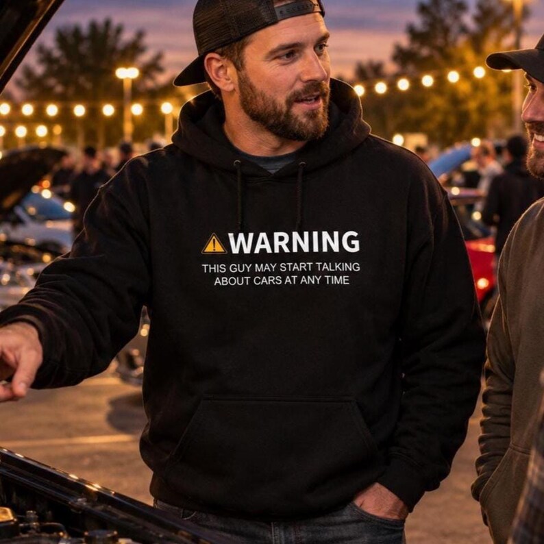 Man in a black car guy warning hoodie talking to friends next to an open engine bay at an evening car meet